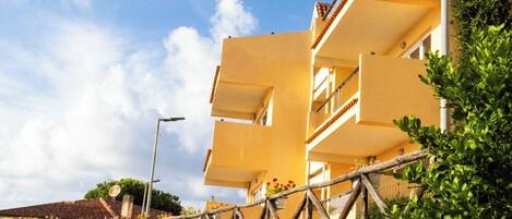 A multi-story building with balconies, a paved pathway, and a variety of potted plants.