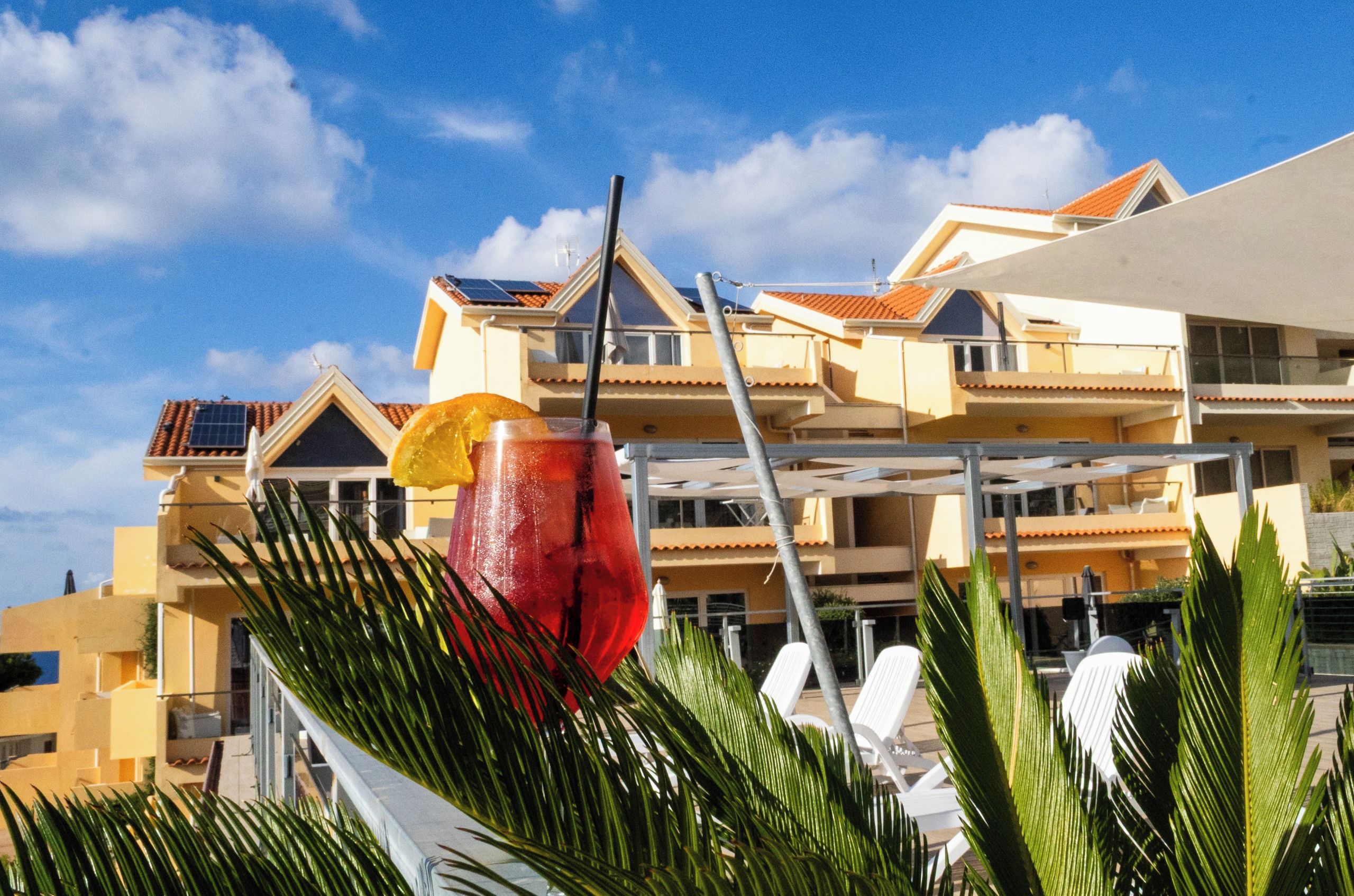 Un hotel con diversi balconi, cielo sereno e una pianta tropicale in primo piano.