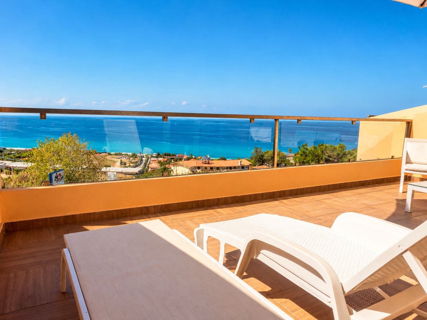 Ein Balkon mit Meerblick, einem Tisch und zwei weißen Stühlen.