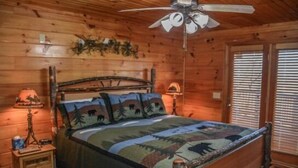 A wooden cabin bedroom with a bed, a nightstand, a lamp, and a ceiling fan. - Captain Morley`s Mountain Inn (Morganton)