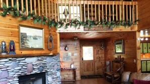 A cozy cabin interior with a stone fireplace, wooden walls, a loft area with a railing, and a dining area with a table and chairs. - Captain Morley`s Mountain Inn (Morganton)
