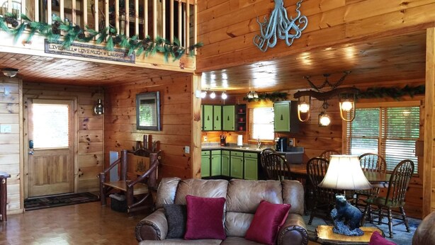 A cozy cabin interior with a leather sofa, wooden dining table, and a kitchen area with green cabinets. - Captain Morley`s Mountain Inn (Morganton)
