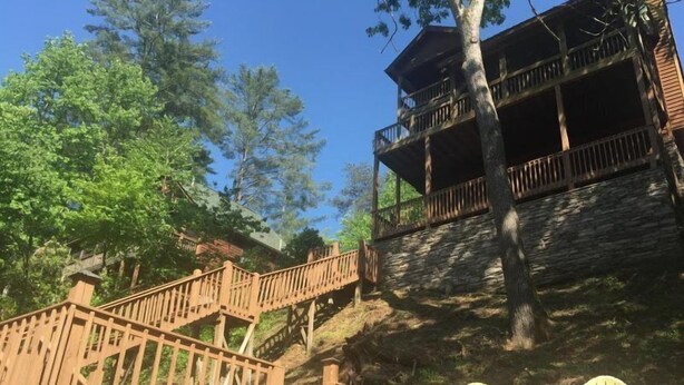 A wooden deck with chairs, a stone staircase, and a building with balconies.