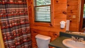 A wooden cabin bathroom with a toilet, a sink, and a window with blinds.