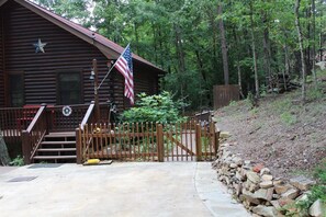 A log cabin with a porch, a flag, and a stone wall.