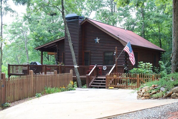A rustic log cabin with a porch, a flag, and a staircase leading to the entrance.