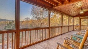 A covered porch with wooden railings and benches, offering a view of a forested landscape. - Paradise Lodge (Blue Ridge)