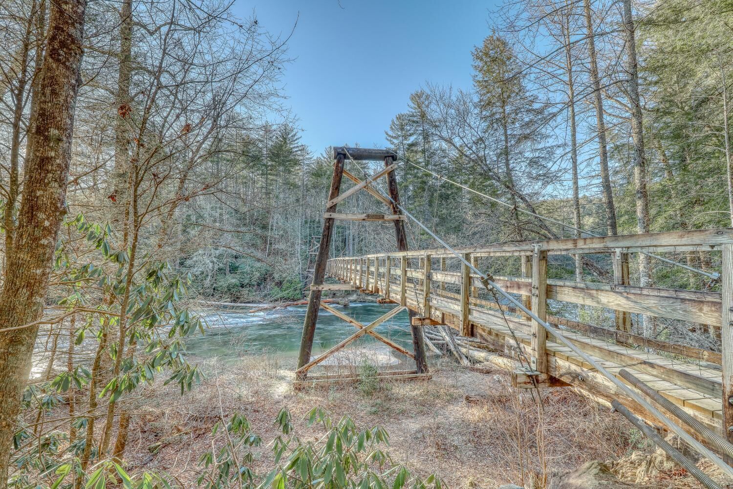 A wooden suspension bridge over a river, surrounded by trees.