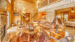 A cozy log cabin interior with a fireplace, leather sofa, and a high ceiling with wooden beams. - Paradise Lodge (Blue Ridge)