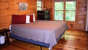 A wooden cabin bedroom with a bed, a dresser, and a window with a view of trees. - Indian Rock Lake (Blue Ridge)