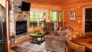 A cozy cabin interior with a stone fireplace, wooden walls, a ceiling fan, and a comfortable seating area. - Indian Rock Lake (Blue Ridge)