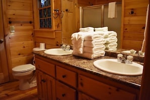 A wooden cabin bathroom with two sinks, a toilet, and a stack of towels.