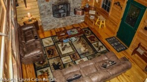 A cabin interior with a stone fireplace, leather sofas, a television, and a green door.