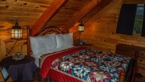 A cozy log cabin bedroom with a bed, two nightstands, a small table, and two wall-mounted lanterns.