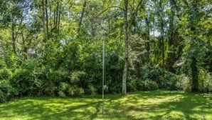 A grassy area with a metal pole and a sign, surrounded by dense green foliage.