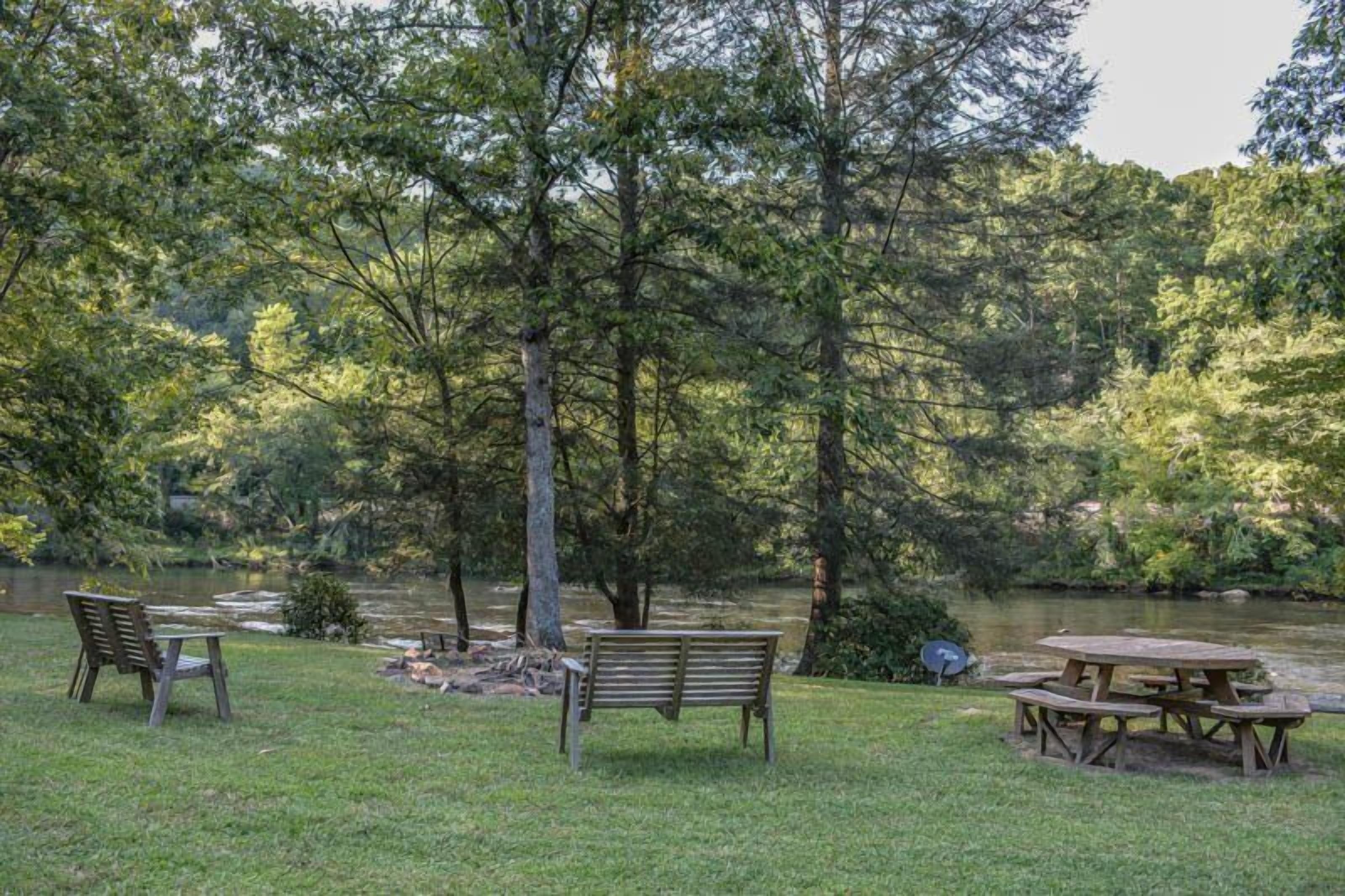A park with a picnic table and benches near a pond surrounded by trees.