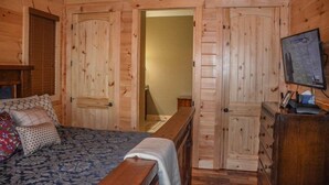 Een slaapkamer in een houten hutje met een bed, een dressoir en een televisie op een dressoir.