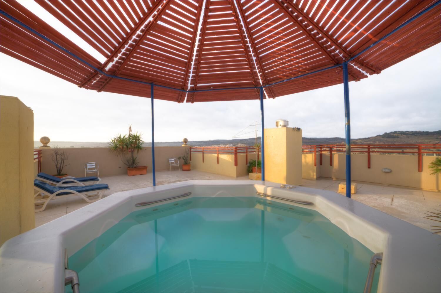 A rooftop swimming pool with lounge chairs and potted plants.