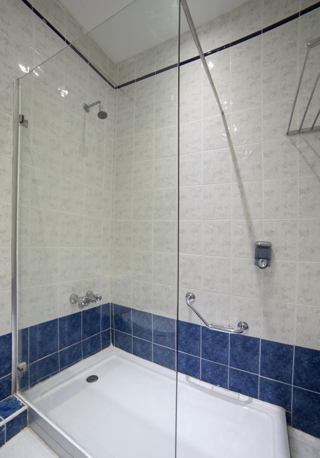 A bathroom with a glass-enclosed shower, a bathtub, and blue-tiled walls.
