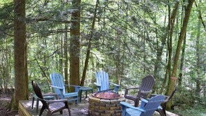 A circular fire pit surrounded by six Adirondack chairs on a wooden deck in a forest. - Tranquilidad (Blue Ridge)