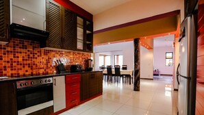 Une cuisine moderne aux couleurs rouge et noir, un coin repas avec une table et des chaises, et une grande colonne au centre.