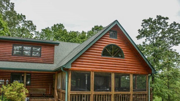 Une cabane en rondins dotée d’une véranda et de grandes fenêtres.