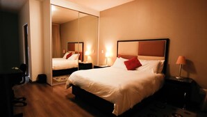 Une chambre d’hôtel avec un grand lit, un bureau et une chaise. Il y a un miroir au mur et une lampe sur le bureau.