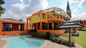 Un immeuble à plusieurs étages doté d’une piscine, d’un patio couvert et, au loin, d’un clocher d’église.