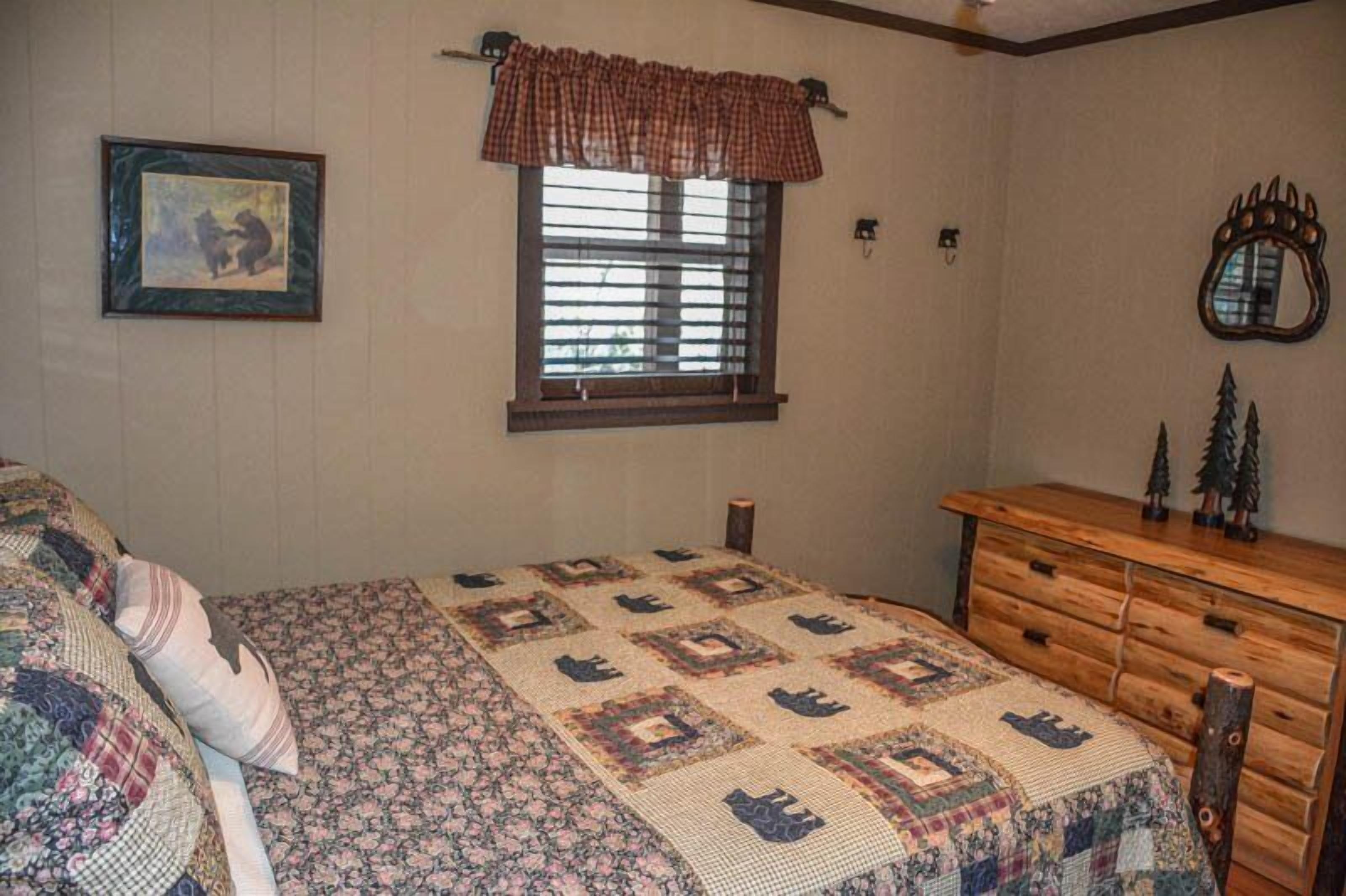Une chambre à coucher avec un lit, une commode, une fenêtre avec des stores, un tableau encadré et un miroir sur le mur.