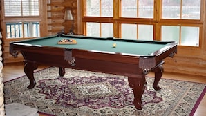 Une table de billard dans une pièce aux murs en bois et aux grandes fenêtres.