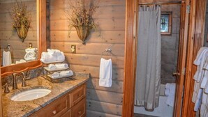 A wooden cabin bathroom with a granite sink, two wall-mounted lights, a mirror, and a towel rack. - Falling Waters Lodge (Ellijay)