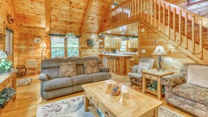 A cozy cabin interior with a wooden staircase, a living room with a sofa and chairs, a kitchen area, and a dining table. - Lucilles Creekside Hideaway (Blue Ridge)