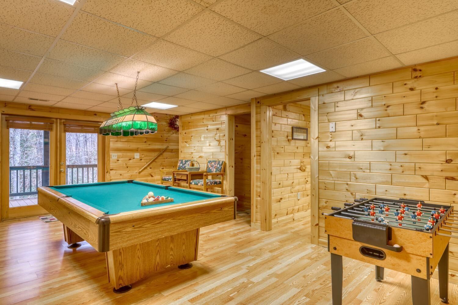 A wooden-floored room with a pool table and a foosball table.