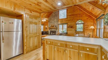 A wooden cabin interior with a kitchen featuring a stone fireplace, wooden cabinets, and a large island.