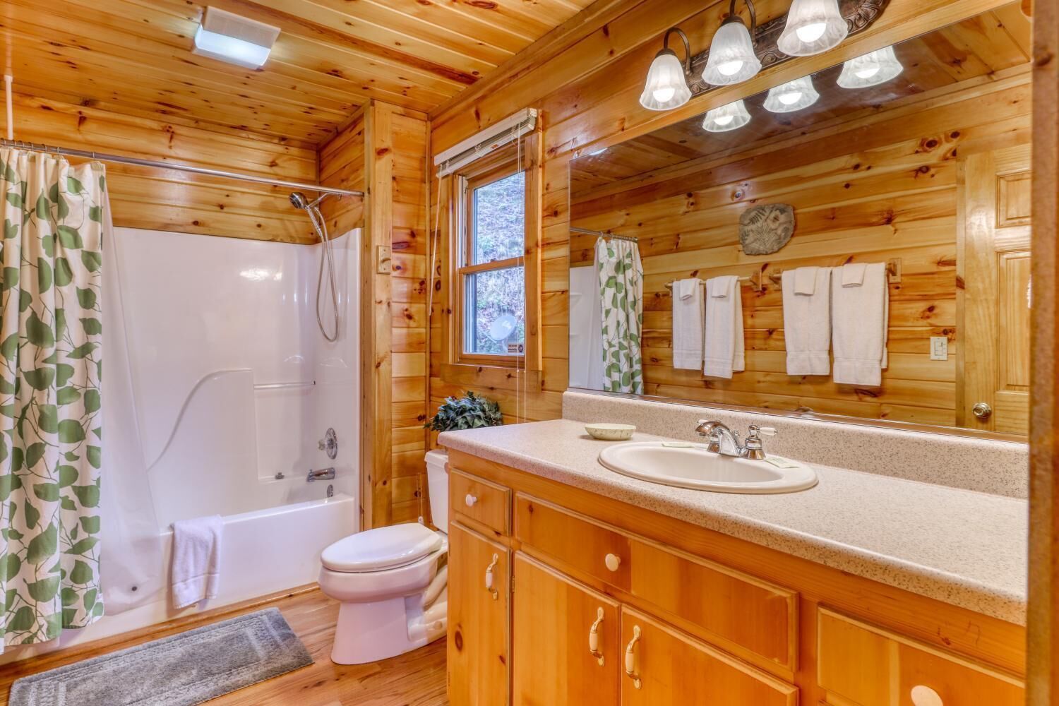 A wooden cabin bathroom with a shower, toilet, sink, and wooden cabinets.