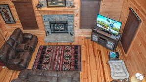 A log cabin interior with a stone fireplace, leather sofas, a television, and a rug. - Harleys River Retreat (Ellijay)