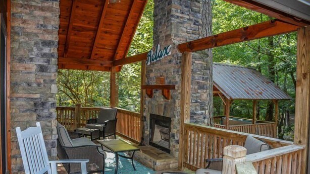 A covered outdoor seating area with stone walls, wooden deck, and a fireplace. - Harleys River Retreat (Ellijay)