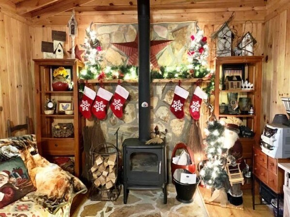 A cozy cabin interior with a stone fireplace, Christmas stockings, a small Christmas tree, and a bed with a floral bedspread. - Alone At Last (Blue Ridge)