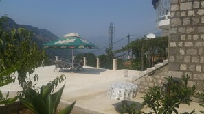 An outdoor patio area with a table and chairs, a green umbrella, and a view of mountains.