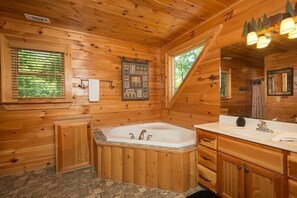 A wooden cabin bathroom with a large bathtub, wooden cabinets, and a window with blinds.