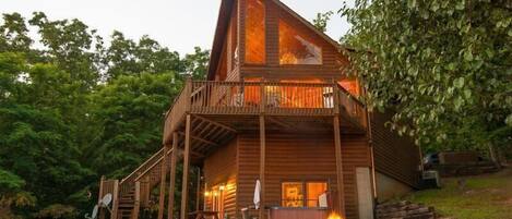 A wooden cabin with a balcony, a fire pit, and a satellite dish.