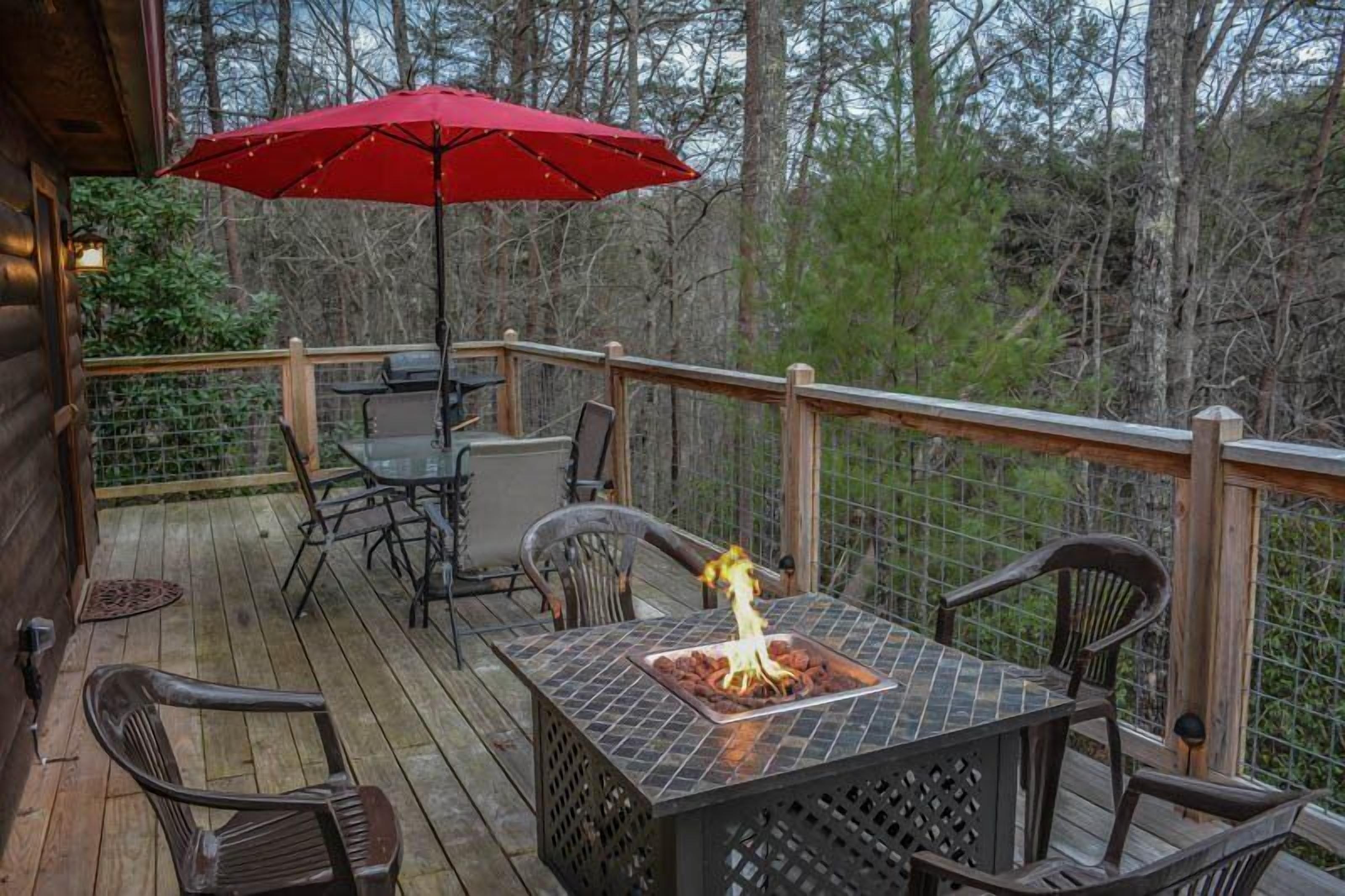 A wooden deck with a table and chairs, a red umbrella, and a fire pit.