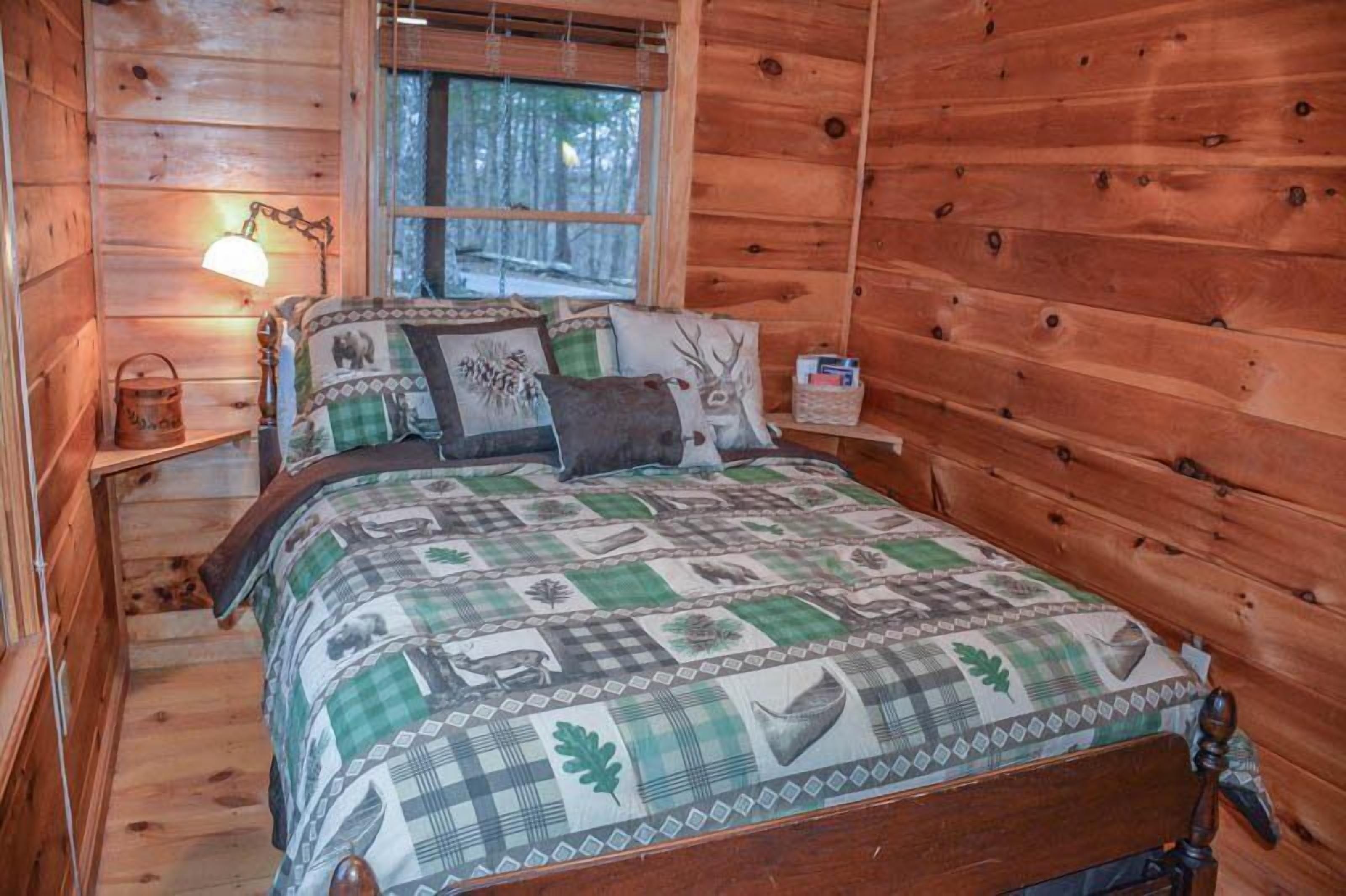 A wooden cabin bedroom with a bed, a nightstand, a lamp, and a window.