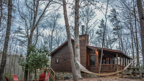 Una rustica baita di legno con veranda e amaca, immersa tra gli alberi.