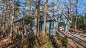 A rustic cabin with a stone foundation, a large garage door, and a staircase leading to a wooden deck.