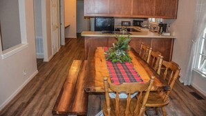 A dining area with a wooden table, benches, and chairs. There is a kitchen in the background with wooden cabinets and appliances.
