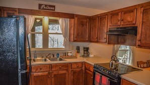 A kitchen with wooden cabinets, a refrigerator, a stove, and a window with curtains.