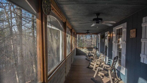 A covered porch with wooden flooring, a ceiling fan, and several rocking chairs.
