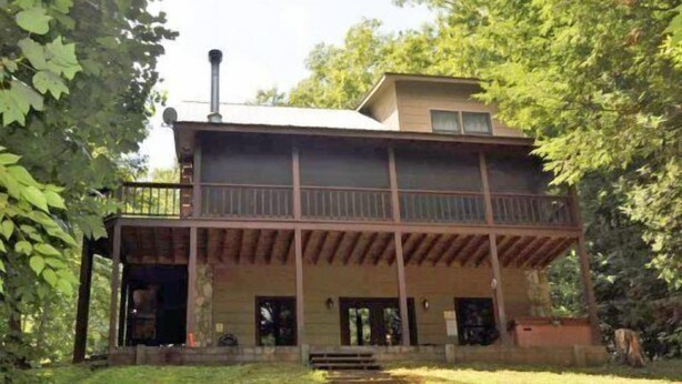 A two-story wooden cabin with a balcony, surrounded by trees. - Rising Trout (Epworth)