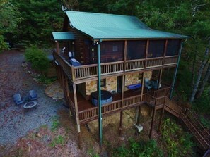 Une cabane en rondins à deux étages, dotée d’un balcon, d’un espace salon extérieur et d’une cheminée en pierre.
